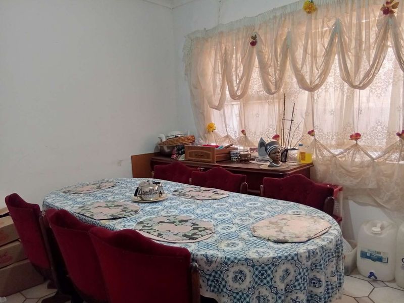 A functional dining room featuring tiled flooring and a large window with decorative curtains, providing a bright and practical space for family meals.