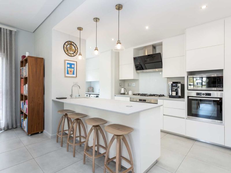 Modern kitchen featuring a central island, sleek white cabinetry, integrated appliances, gas hob, and contemporary pendant lighting with neutral tiled flooring.