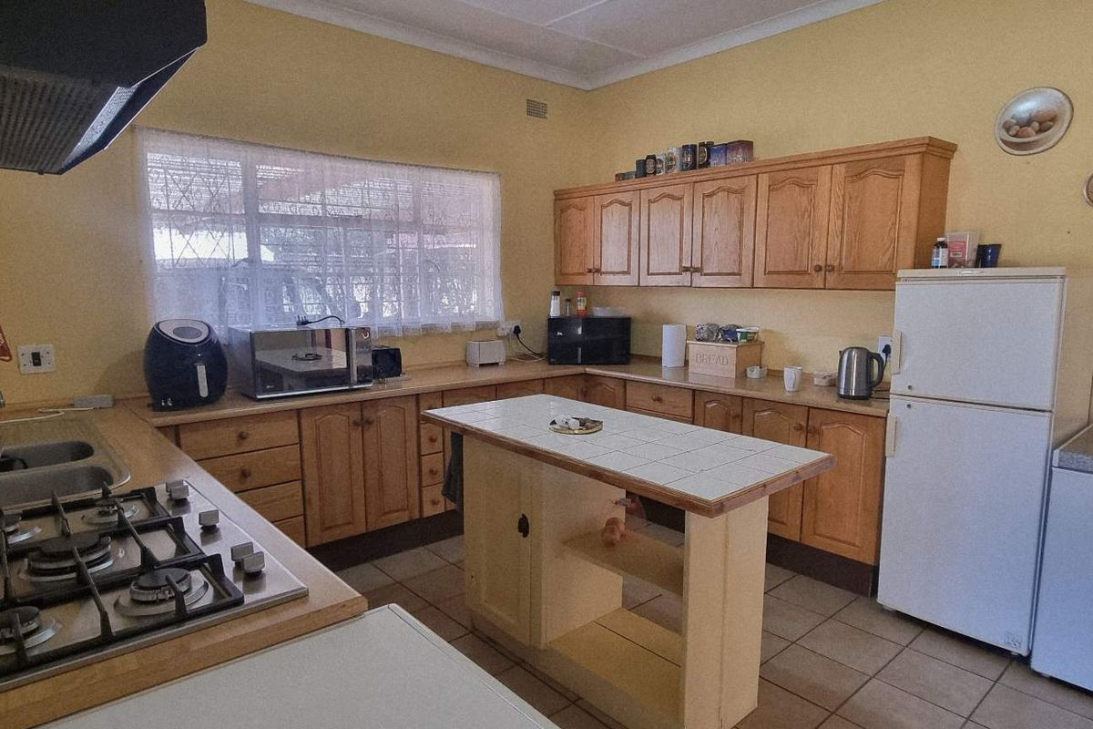 A functional kitchen featuring wooden cabinetry, a gas hob with extractor fan, a central tiled island, and tiled flooring.