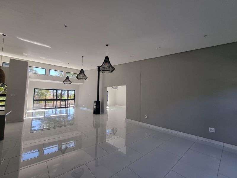 Spacious, modern open-plan living area featuring high ceilings, large windows, polished porcelain tiles, and a sleek freestanding fireplace.