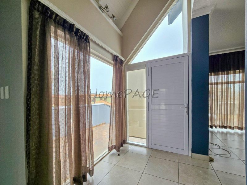 Bright living area featuring vaulted ceilings, tiled flooring, and direct access to an outdoor balcony through a modern aluminium glass door.