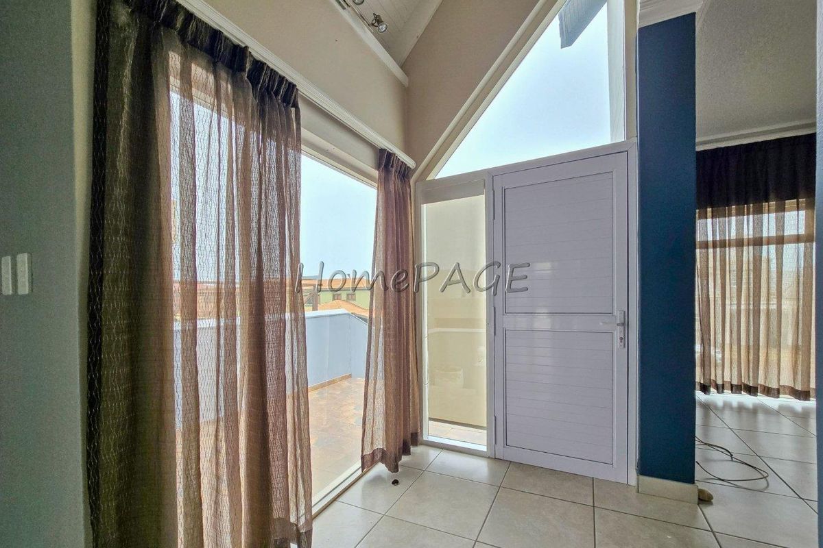 Bright living area featuring vaulted ceilings, tiled flooring, and direct access to an outdoor balcony through a modern aluminium glass door.