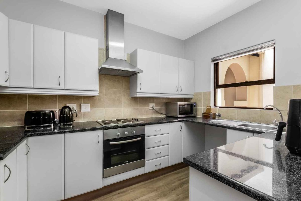 A functional kitchen featuring white cabinetry, granite countertops, a built-in oven, hob, and stainless steel extractor fan with tiled splashbacks.
