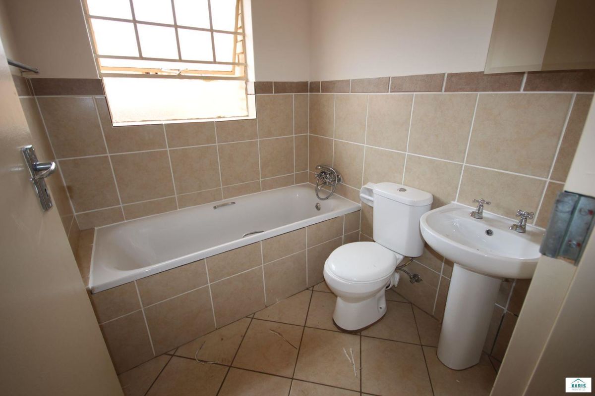A functional bathroom featuring a built-in bathtub, pedestal basin, and toilet with neutral wall tiling and tiled flooring.