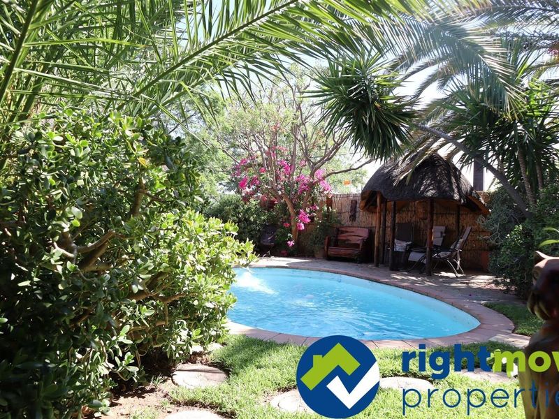 A private outdoor pool area featuring a thatched gazebo, paved surround, and established garden landscaping, providing a tranquil setting for relaxation.