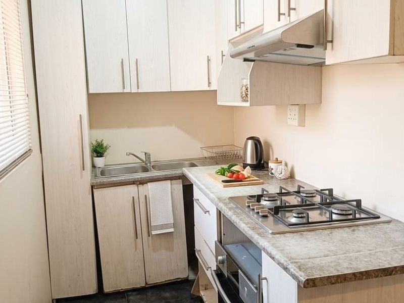 Compact, functional kitchen featuring light wood-grain cabinetry, stone-look countertops, a gas hob, built-in oven, and dark tiled flooring.