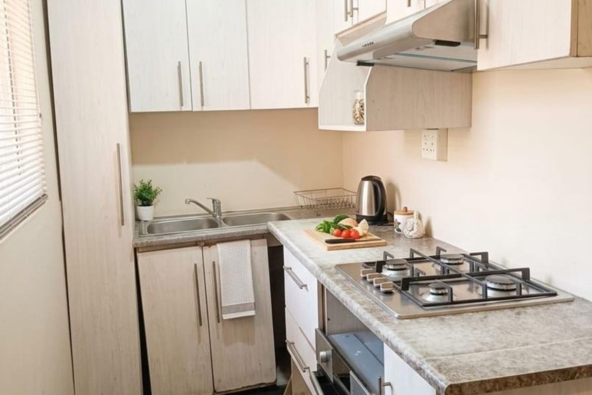 Compact, functional kitchen featuring light wood-grain cabinetry, stone-look countertops, a gas hob, built-in oven, and dark tiled flooring.