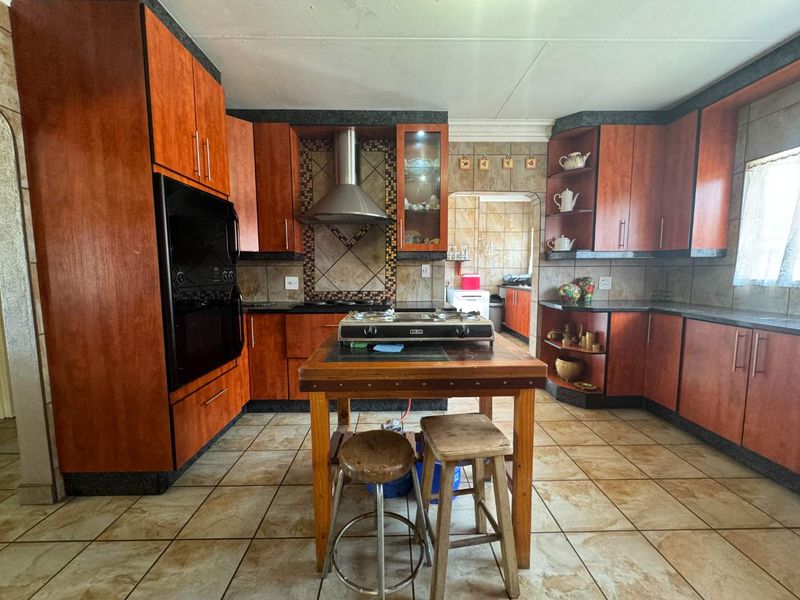 A spacious kitchen featuring wood-finish cabinetry, built-in oven, extractor fan, and tiled surfaces, offering a functional layout with potential for modern updates.