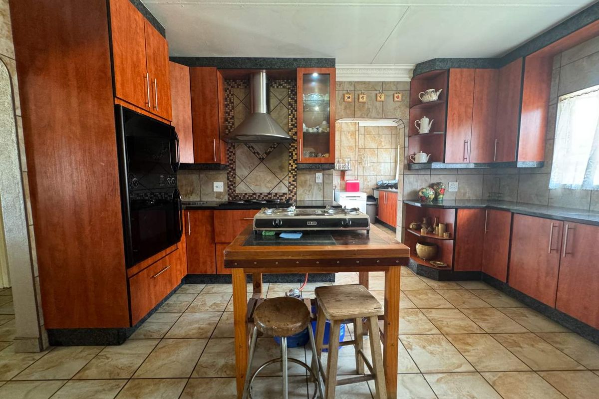 A spacious kitchen featuring wood-finish cabinetry, built-in oven, extractor fan, and tiled surfaces, offering a functional layout with potential for modern updates.