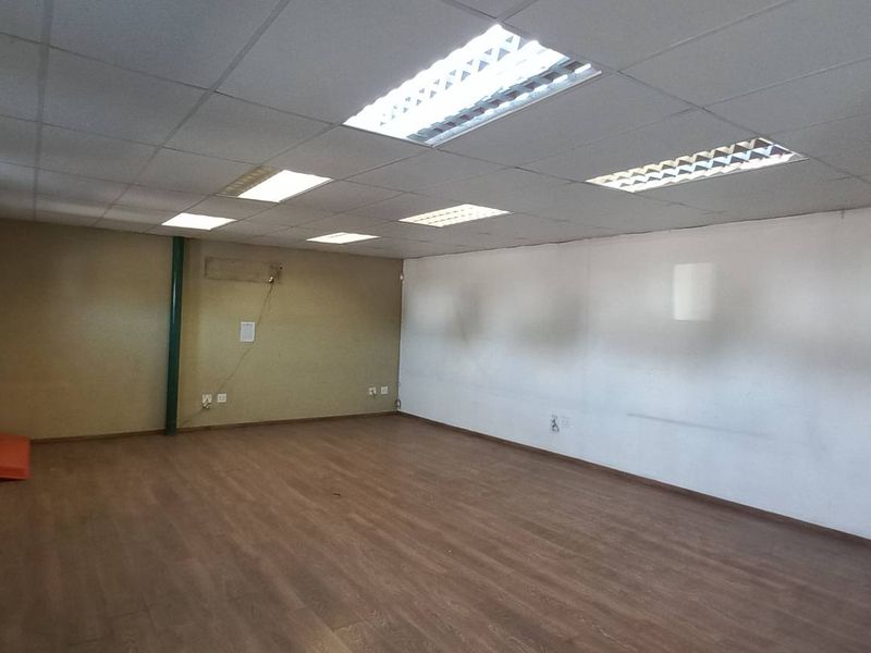 Spacious open-plan industrial office area featuring wood-look flooring, suspended ceiling tiles, recessed lighting, and a secure metal security gate at the entrance.