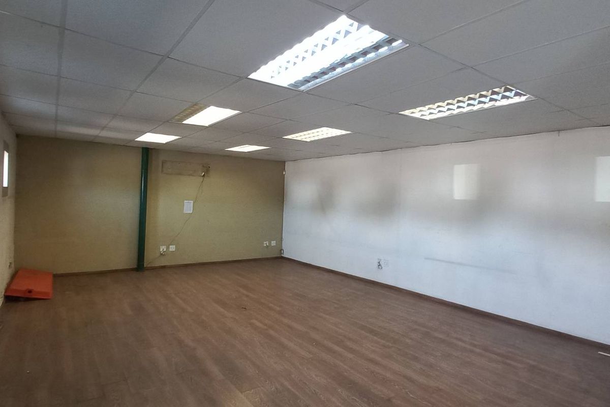 Spacious open-plan industrial office area featuring wood-look flooring, suspended ceiling tiles, recessed lighting, and a secure metal security gate at the entrance.
