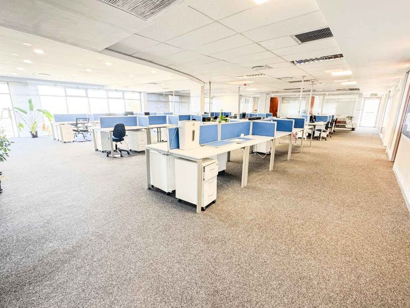 Spacious open-plan office area featuring a suspended ceiling, recessed lighting, air conditioning, and large windows providing ample natural light.