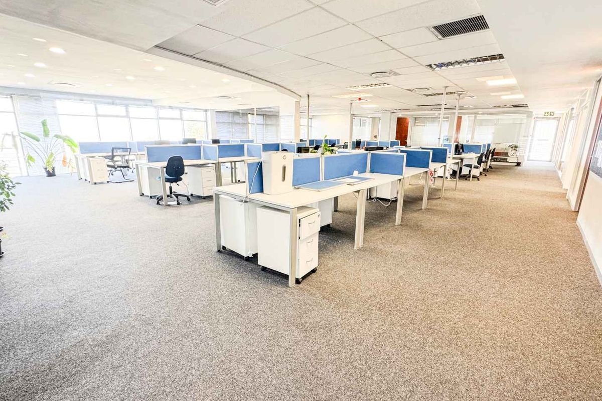 Spacious open-plan office area featuring a suspended ceiling, recessed lighting, air conditioning, and large windows providing ample natural light.