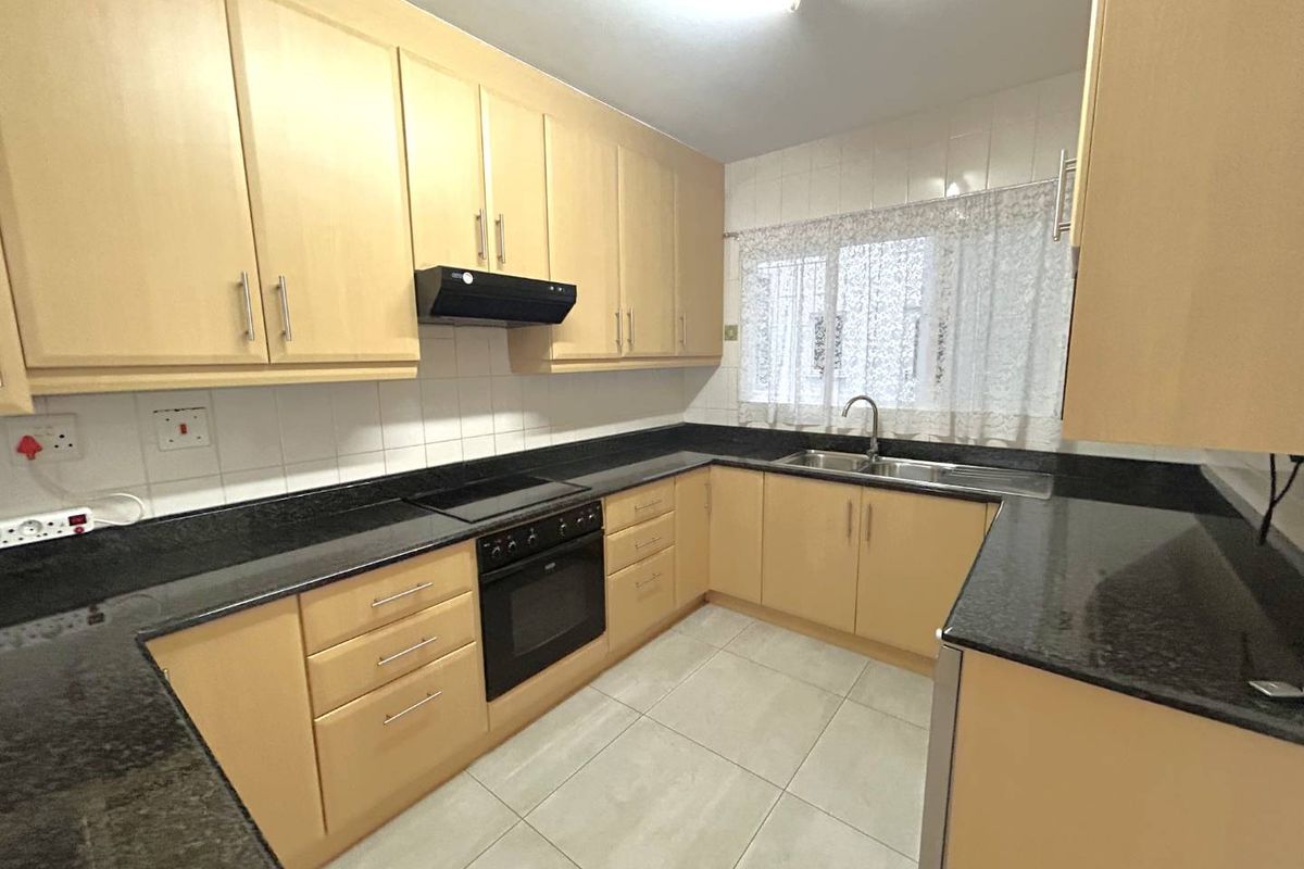 A functional U-shaped kitchen featuring light wood cabinetry, dark granite countertops, built-in oven and hob, and tiled flooring.