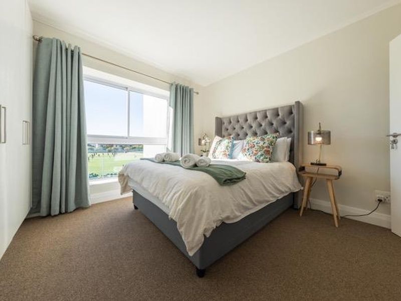 A well-maintained bedroom featuring neutral walls, carpeted flooring, built-in cupboards, and a large sliding window providing natural light and views.