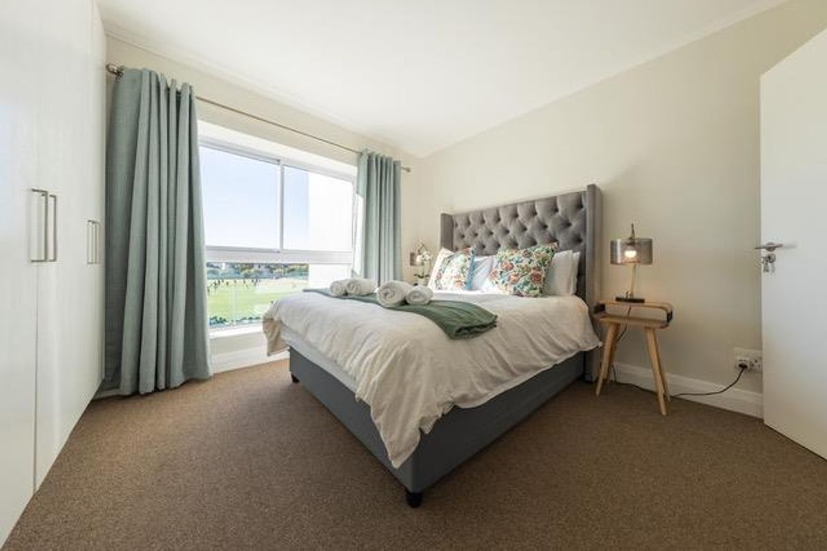 A well-maintained bedroom featuring neutral walls, carpeted flooring, built-in cupboards, and a large sliding window providing natural light and views.