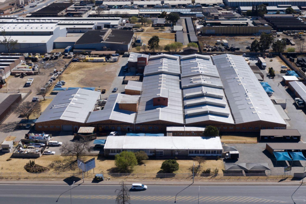 Aerial view of a large industrial facility featuring extensive warehouse space, multiple roof sections, and dedicated parking areas within a secure perimeter.