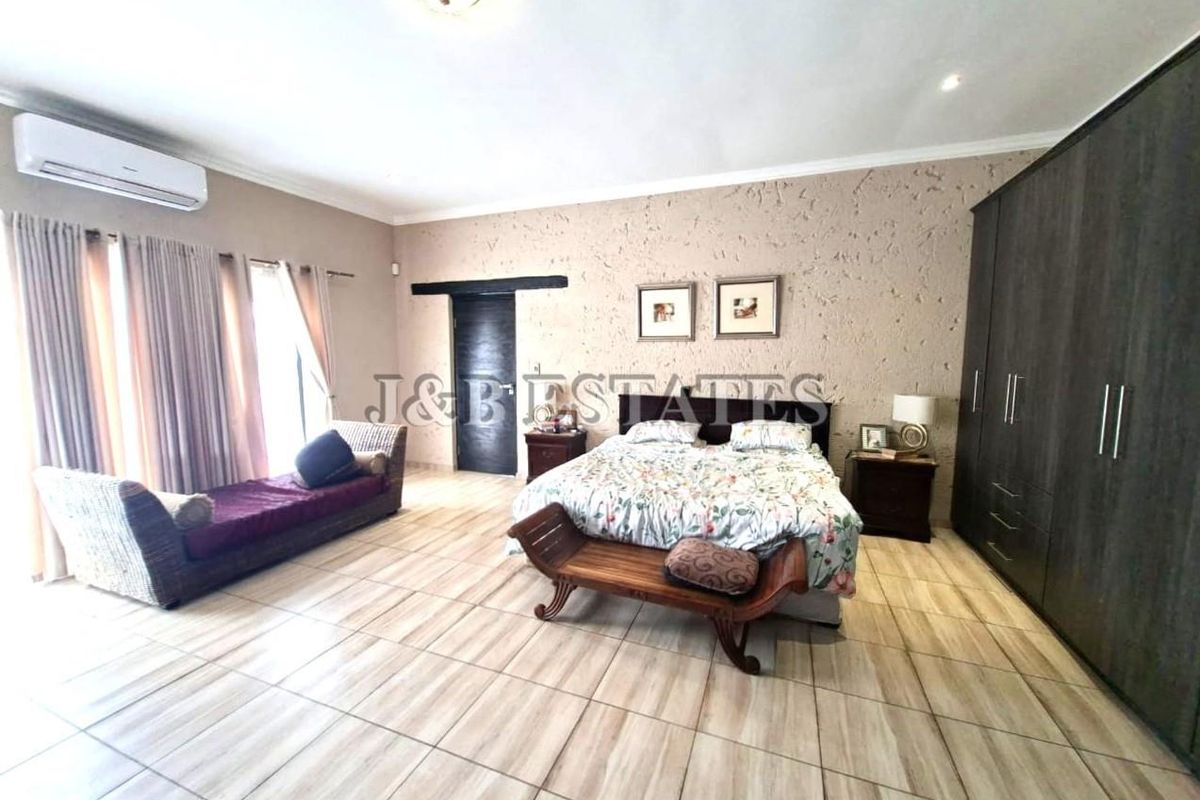 Spacious bedroom featuring tiled flooring, built-in cupboards, textured accent wall, and a wall-mounted air conditioning unit.