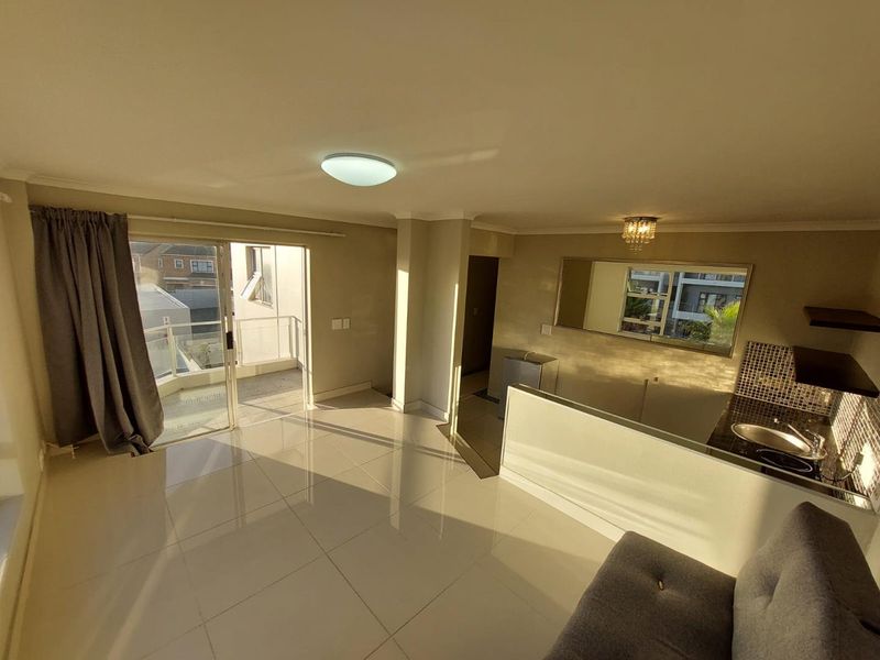 Open-plan living area featuring tiled floors, a compact kitchen with mosaic backsplash, and direct access to a private balcony.