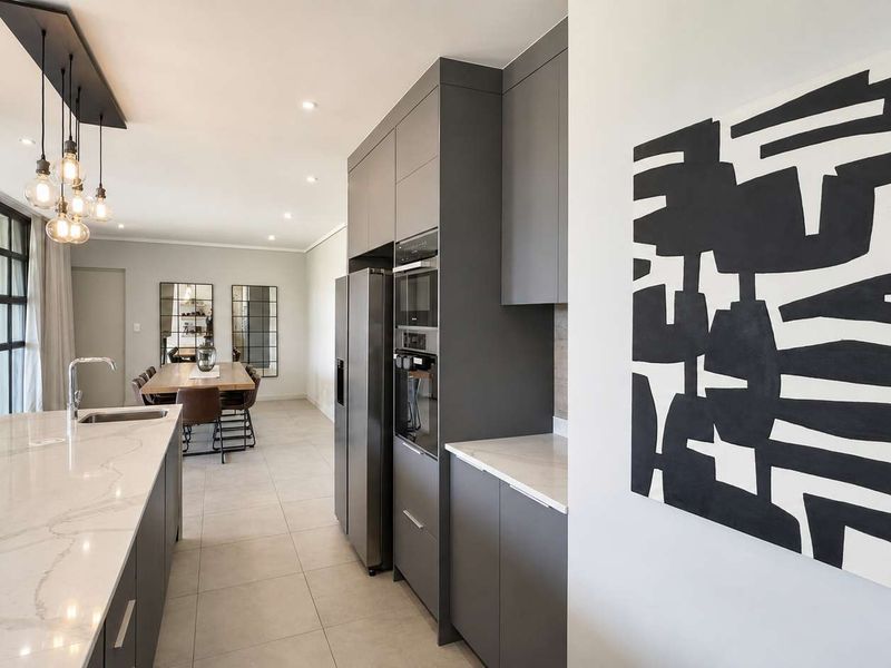 Modern open-plan kitchen and dining area featuring sleek grey cabinetry, stone countertops, a central island, and large sliding doors leading to the outdoors.