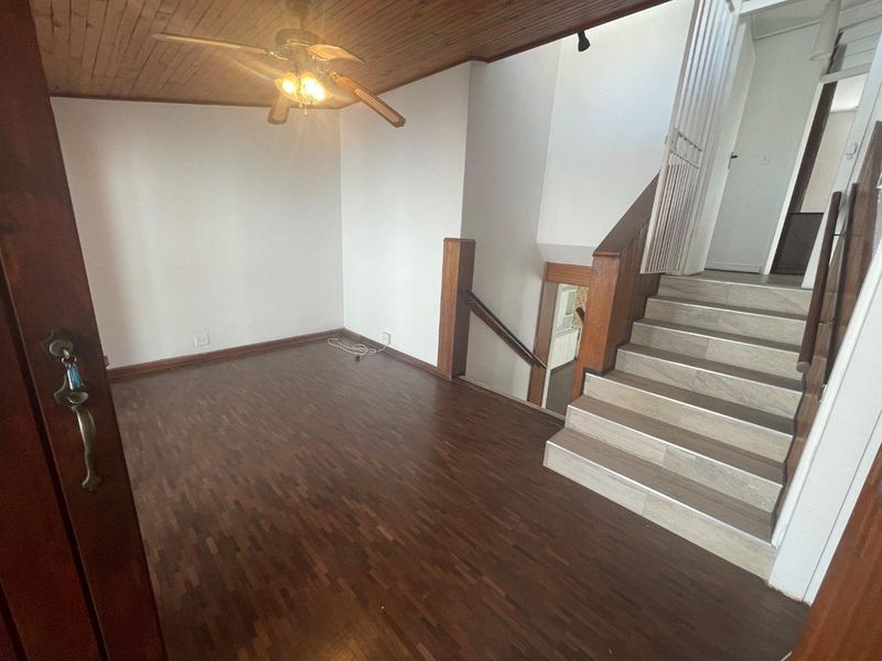 An empty living area featuring parquet flooring, a timber ceiling with a fan, and a staircase leading to the upper level.