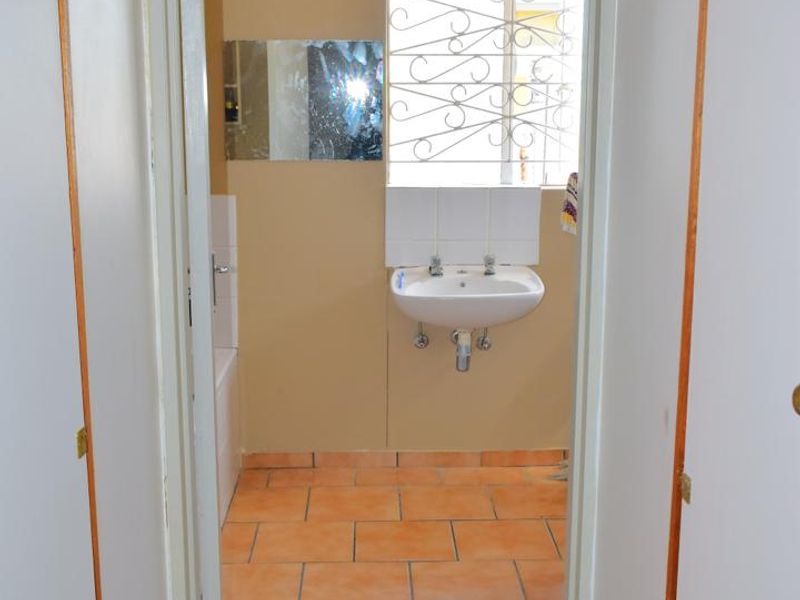 A functional bathroom featuring tiled flooring, a wall-mounted basin, and a bathtub, requiring cosmetic updates to modernize the space.