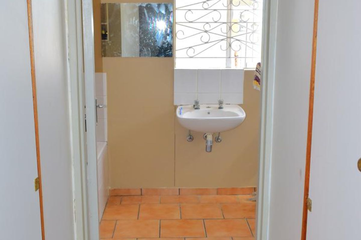 A functional bathroom featuring tiled flooring, a wall-mounted basin, and a bathtub, requiring cosmetic updates to modernize the space.