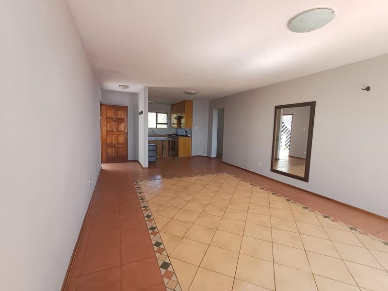Spacious open-plan living and kitchen area featuring tiled flooring, neutral walls, and functional built-in kitchen cabinetry.