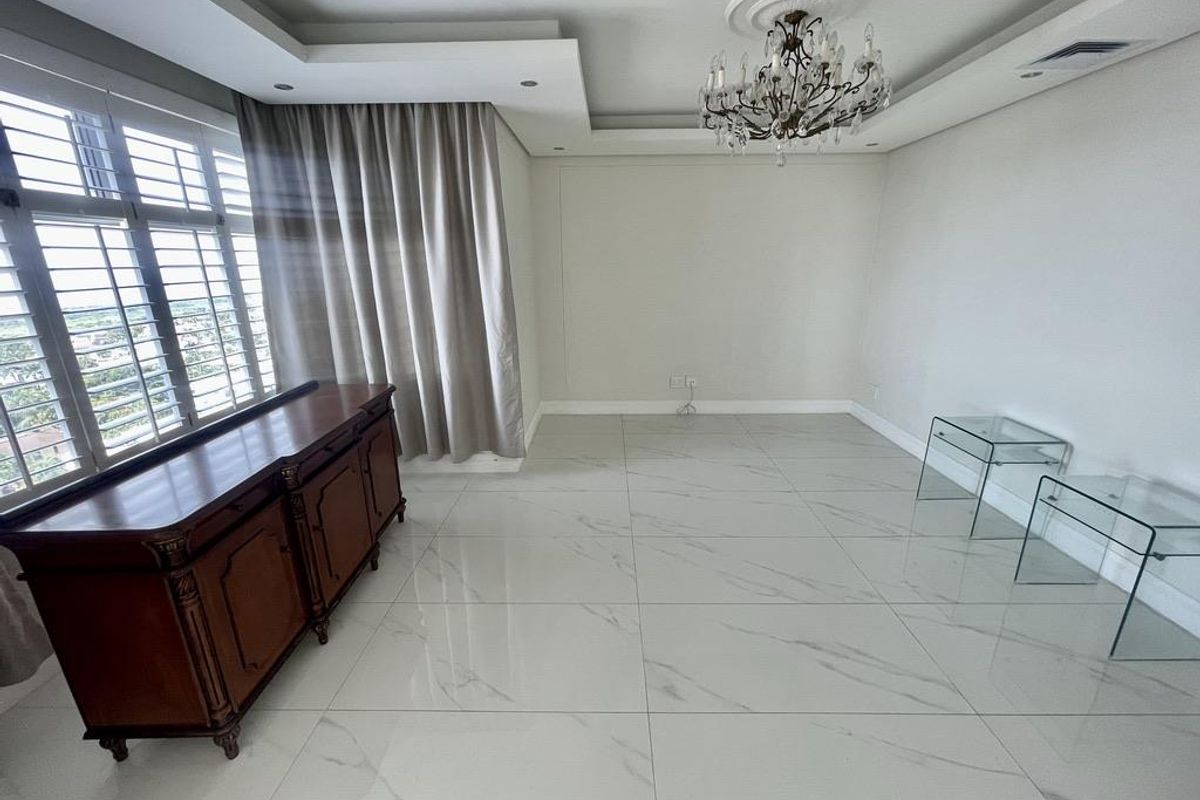 Spacious living area featuring large format marble-look floor tiles, recessed tray ceiling with downlights, decorative chandelier, and plantation shutters.