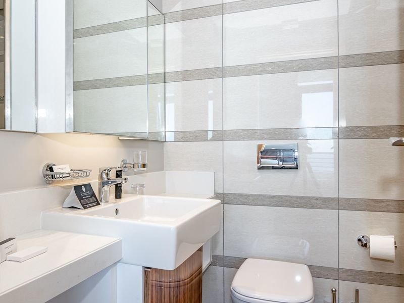Modern bathroom featuring a wall-mounted toilet, integrated vanity basin with chrome fixtures, and a sleek mirrored medicine cabinet with tiled wall finishes.