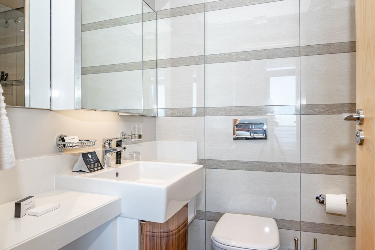 Modern bathroom featuring a wall-mounted toilet, integrated vanity basin with chrome fixtures, and a sleek mirrored medicine cabinet with tiled wall finishes.