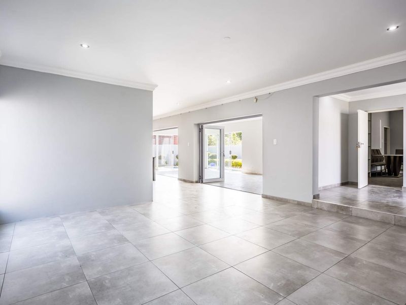 Spacious open-plan living area featuring neutral grey walls, large format floor tiles, recessed lighting, and seamless access to the outdoor patio through bi-fold doors.