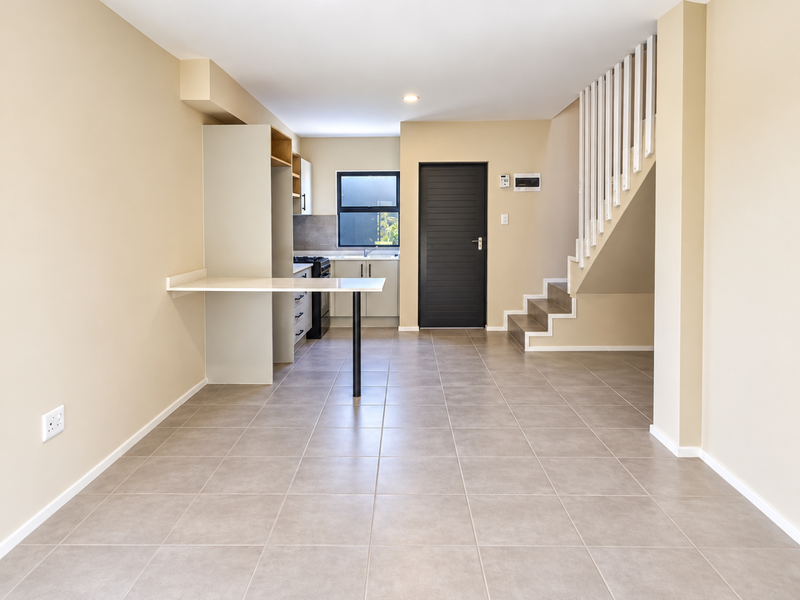 An open-plan living and kitchen area featuring neutral tiled flooring, a modern breakfast bar, built-in cabinetry, and a staircase leading to the upper level.