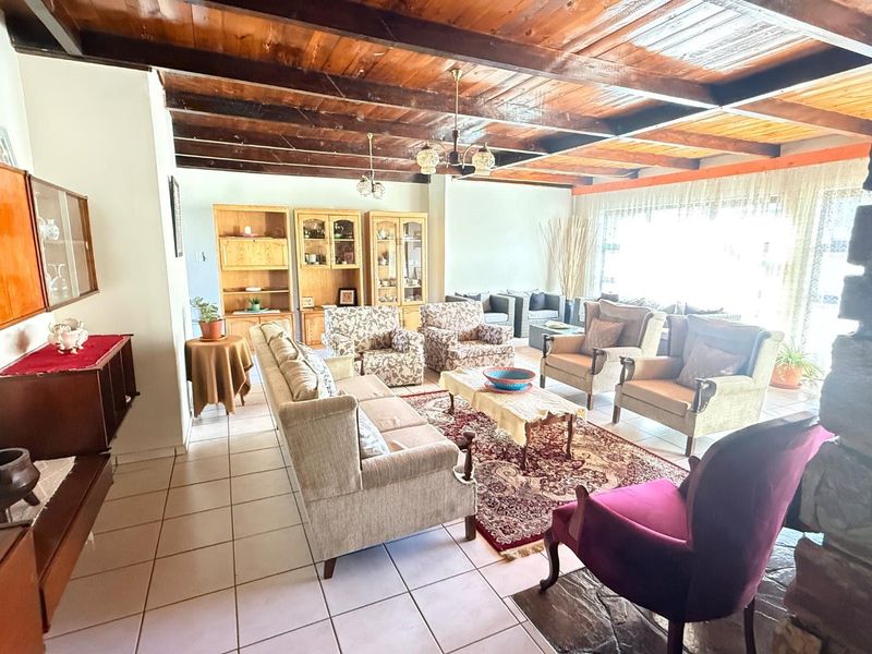 Spacious living room featuring exposed timber ceiling beams, tiled flooring, and a stone fireplace, offering a warm and traditional aesthetic.