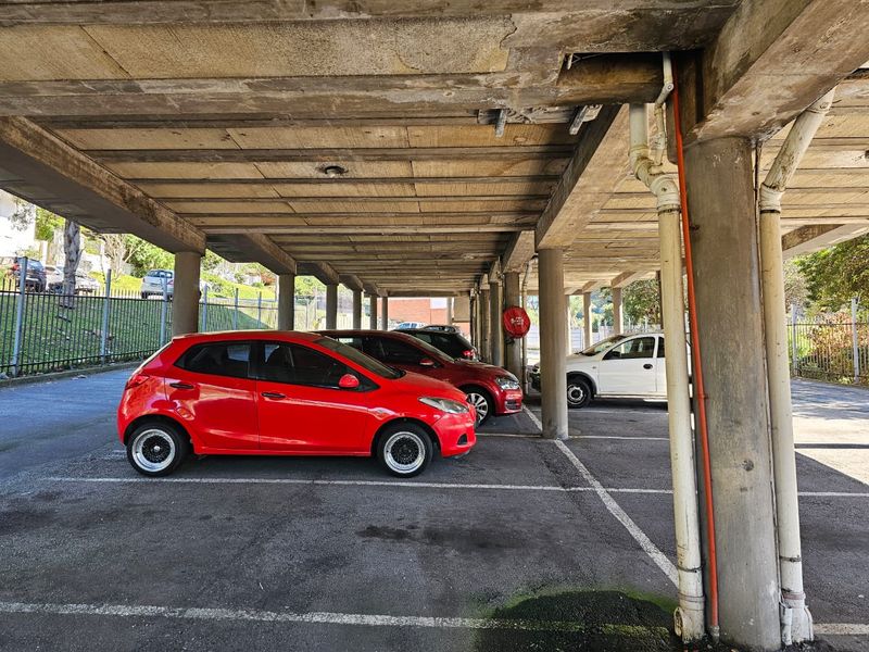 Covered parking area featuring concrete structural pillars and ceiling with marked parking bays.