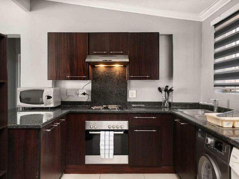 A well-maintained kitchen featuring dark wood cabinetry, granite countertops, a built-in oven, electric hob, extractor fan, and a stainless steel sink.