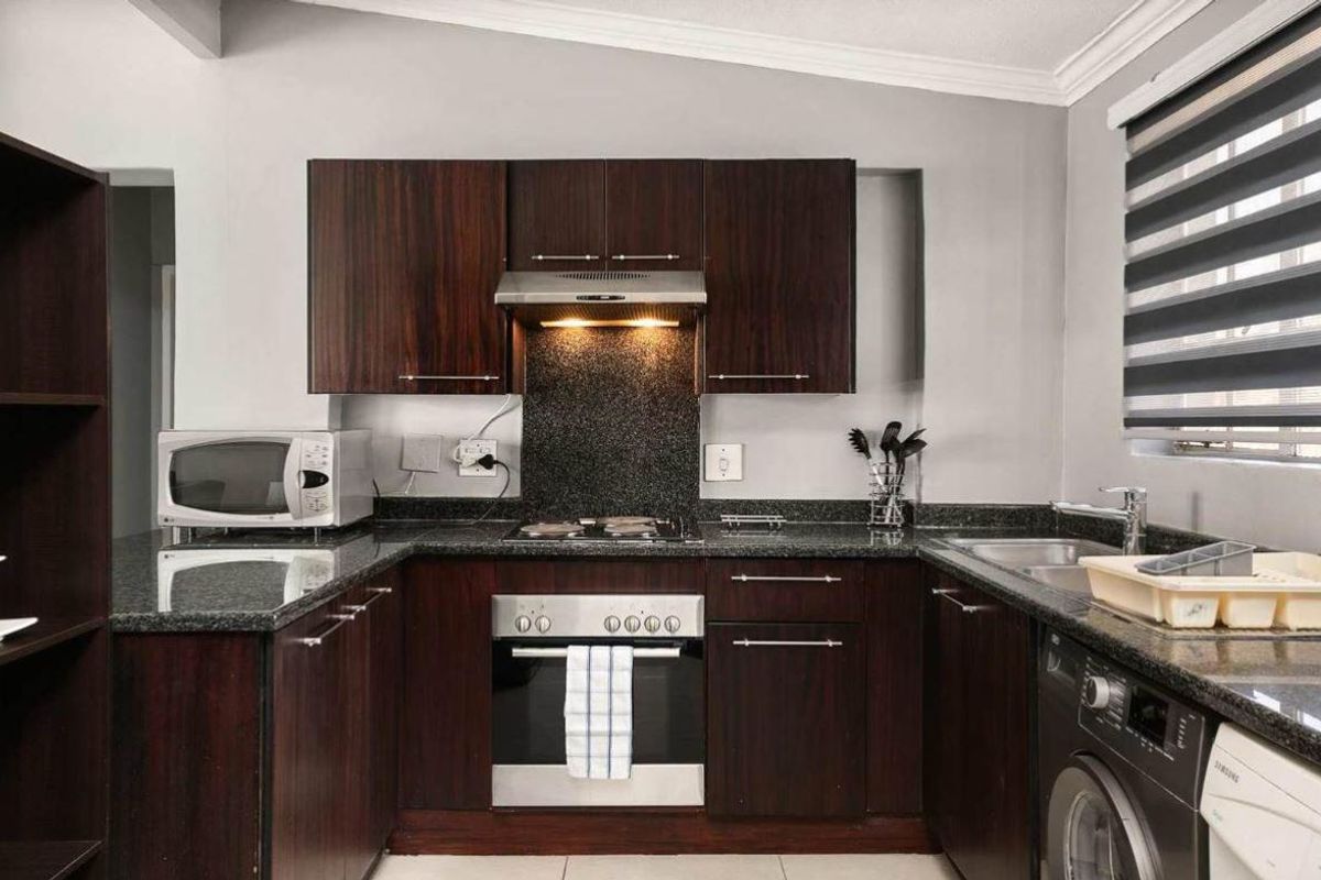 A well-maintained kitchen featuring dark wood cabinetry, granite countertops, a built-in oven, electric hob, extractor fan, and a stainless steel sink.