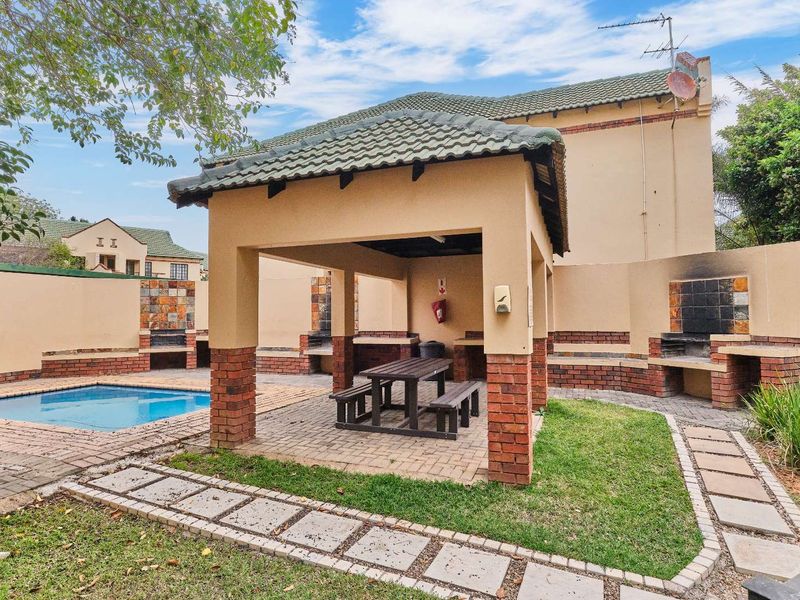 Communal outdoor entertainment area featuring a swimming pool, covered gazebo with built-in braai facilities, and paved garden surrounds.