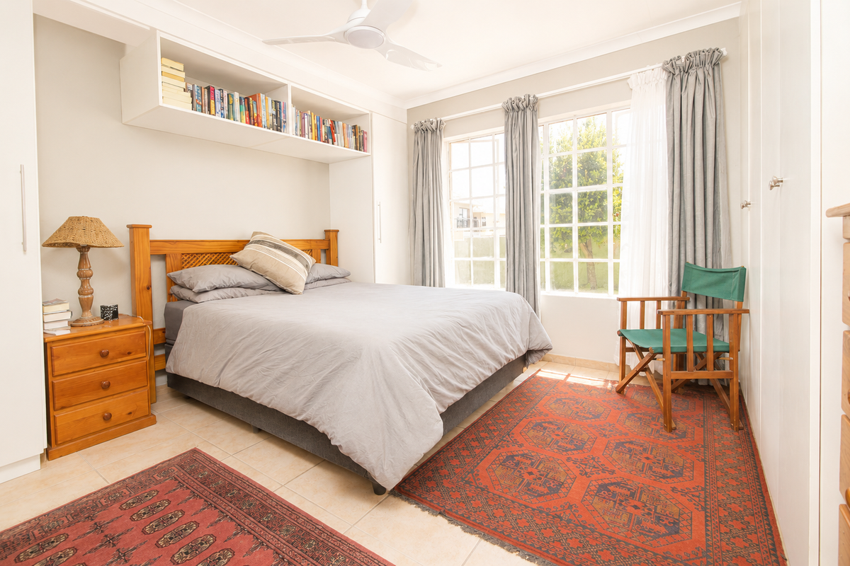 A well-lit bedroom featuring built-in cabinetry, overhead shelving, tiled flooring, and large windows that provide natural light.