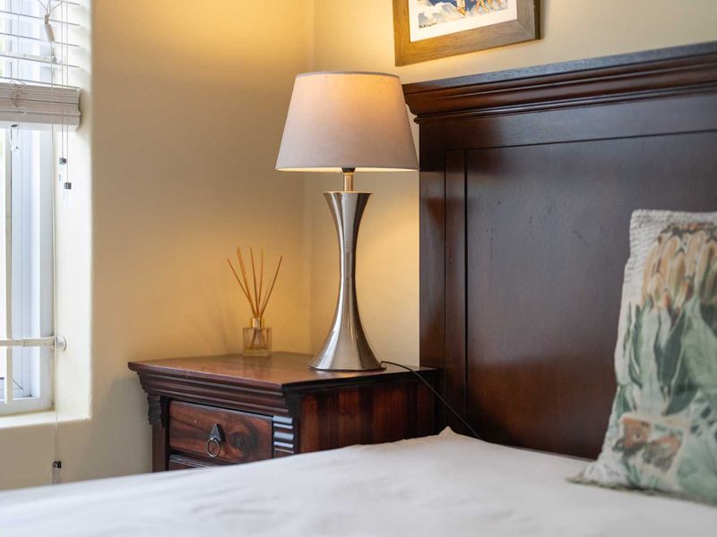A close-up view of a bedroom corner featuring a window with venetian blinds and a dark wood headboard.