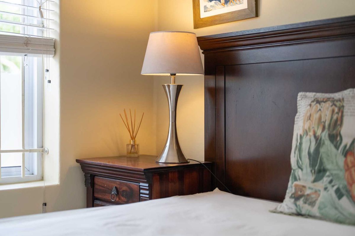 A close-up view of a bedroom corner featuring a window with venetian blinds and a dark wood headboard.