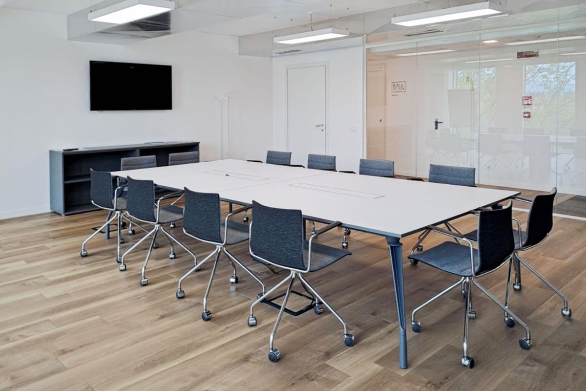 A modern, well-lit office meeting room featuring hardwood flooring, a large conference table, and a glass partition wall for an open, professional workspace.