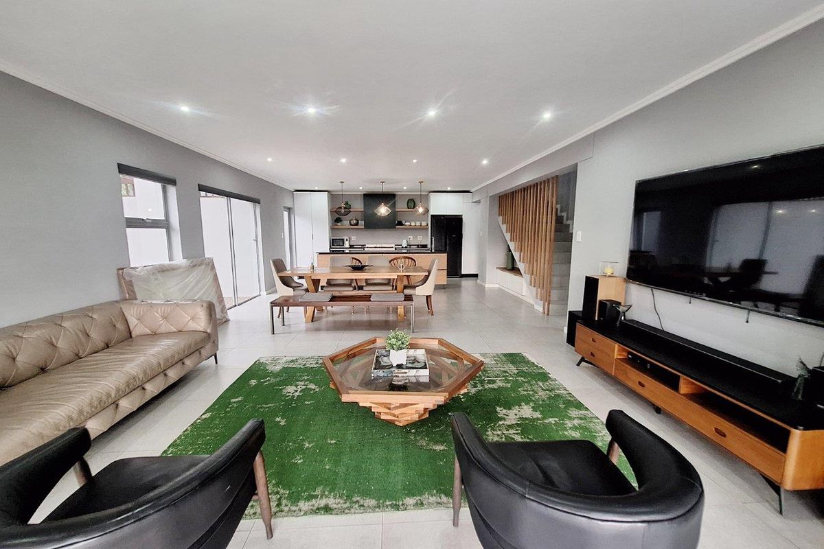 Spacious open-plan living and dining area featuring modern tiled floors, recessed lighting, and a contemporary kitchen with a central island and timber staircase detail.