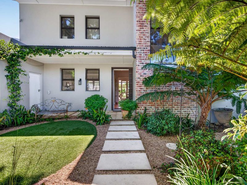 A well-maintained front entrance featuring a paved walkway, artificial lawn, and a distinctive brick chimney facade with established garden landscaping.