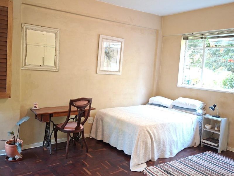 A bedroom featuring classic parquet flooring, large windows providing natural light, and wooden shutters for privacy.