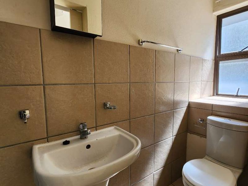 A compact bathroom featuring a pedestal basin, ceramic toilet, and tiled finishes, requiring cosmetic updates to improve its overall condition and appeal.