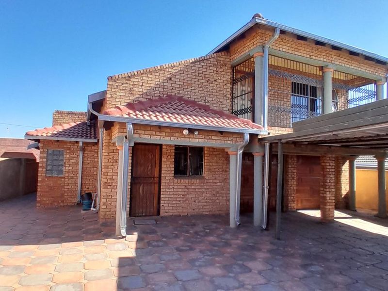 A two-story face brick house featuring a tiled roof, a covered carport, and an upper-level balcony with security gates.
