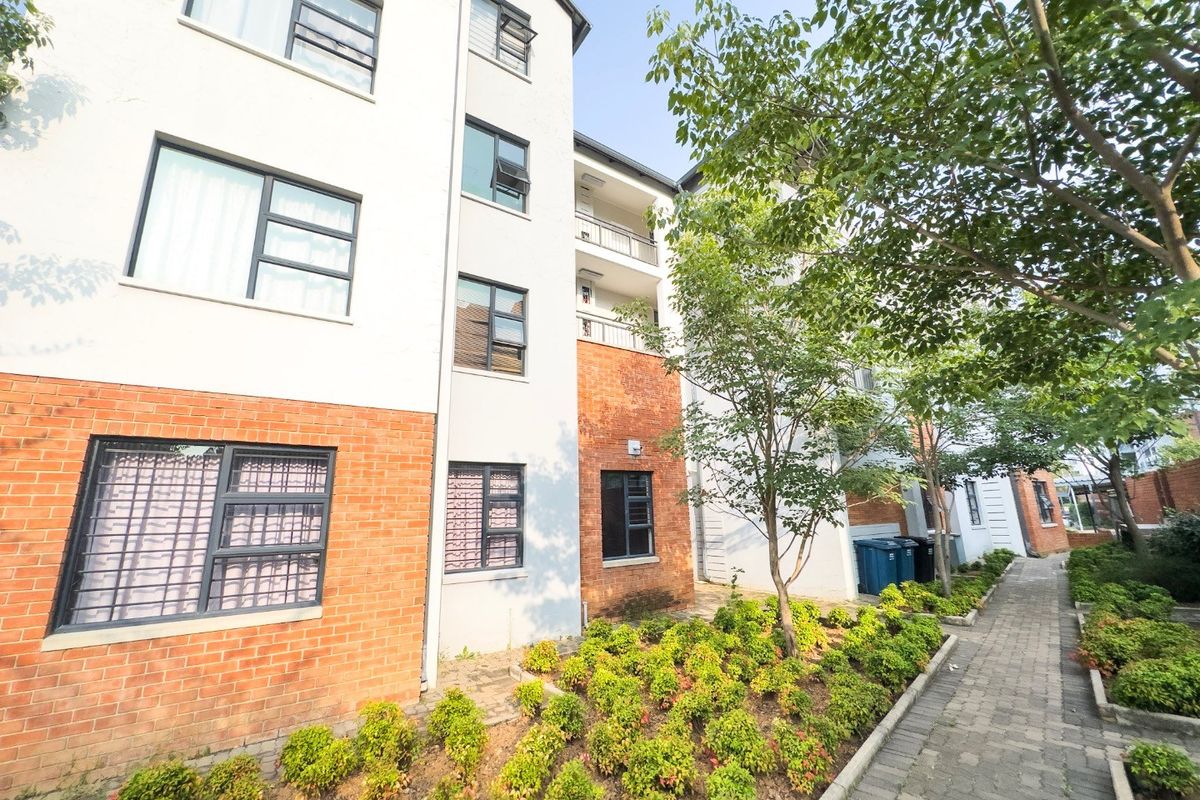 Exterior view of a multi-story apartment building featuring a brick and plaster facade, aluminium windows, balconies, and a well-maintained paved garden walkway.