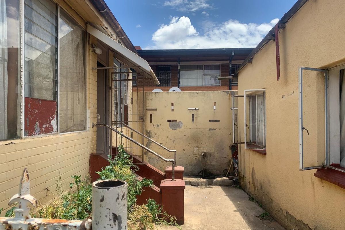 A narrow exterior rear courtyard area featuring concrete paving, weathered brick walls, and metal staircase access to the building.