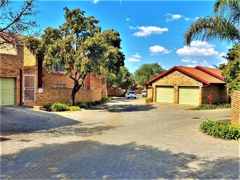 Exterior view of a townhouse complex featuring face brick facades, tiled roofs, and paved driveway access to garages.